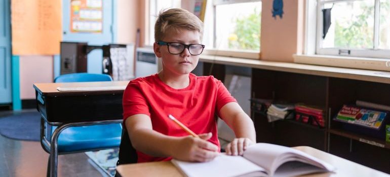 a boy sitting at a table writing something at school