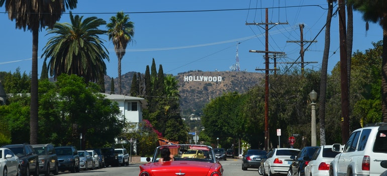 a red car on the street and Hollywood sign in the distance